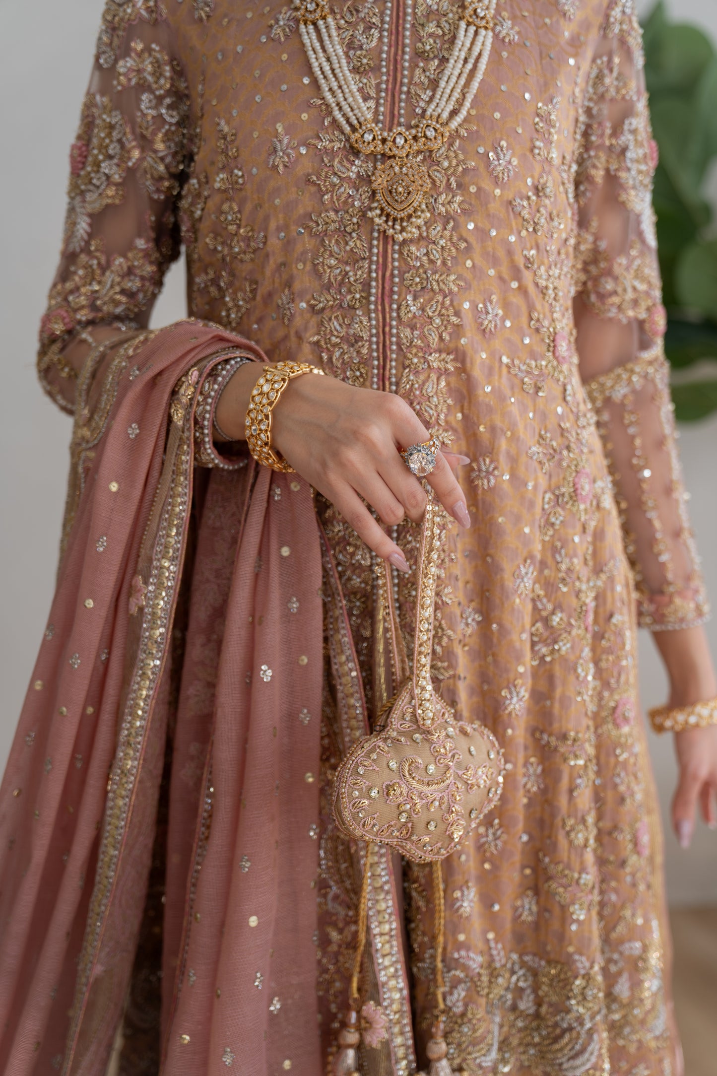 Person wearing a traditional embroidered outfit with a pink dupatta and gold jewelry.