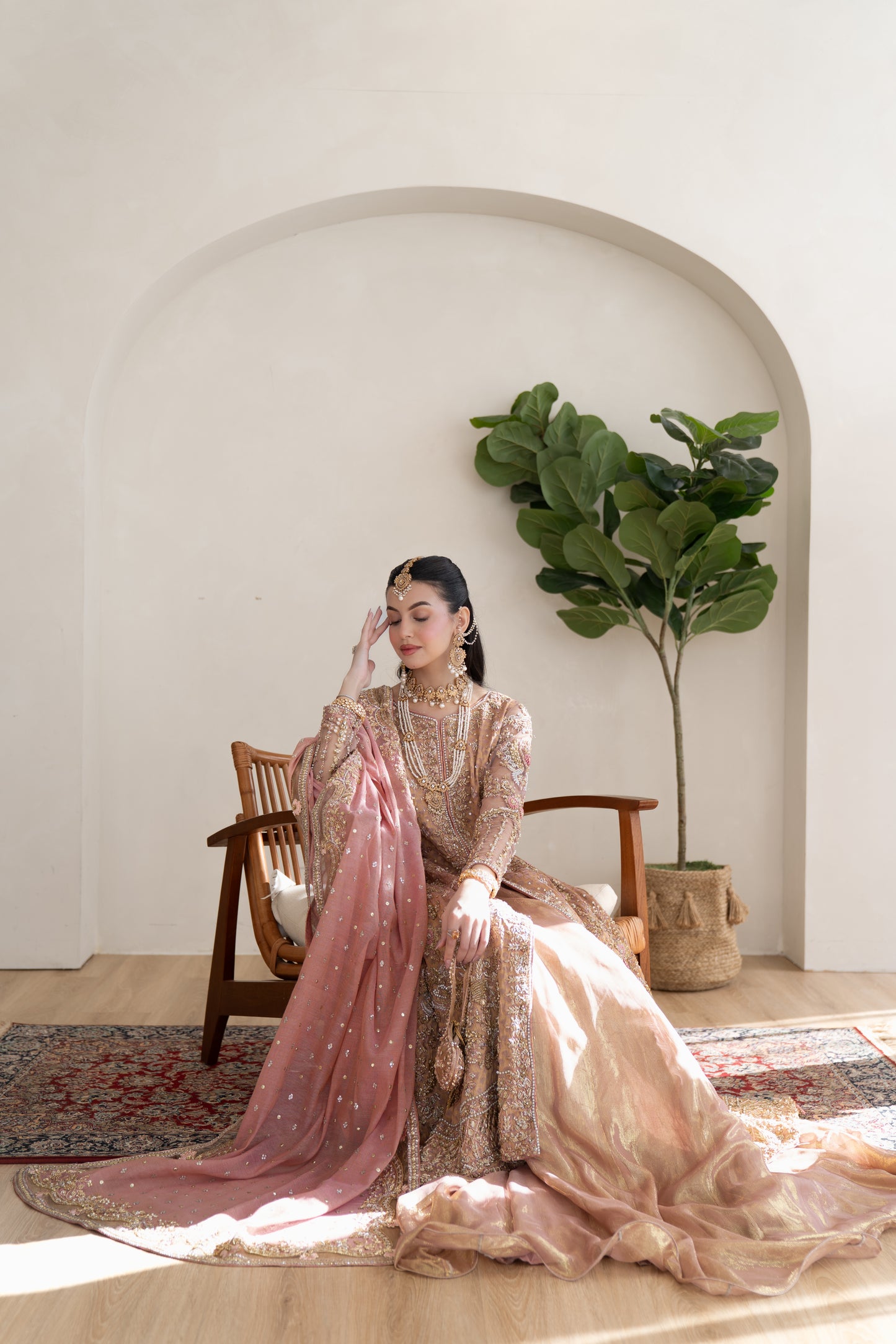 Woman in traditional attire sitting on a wooden chair with a plant in the background